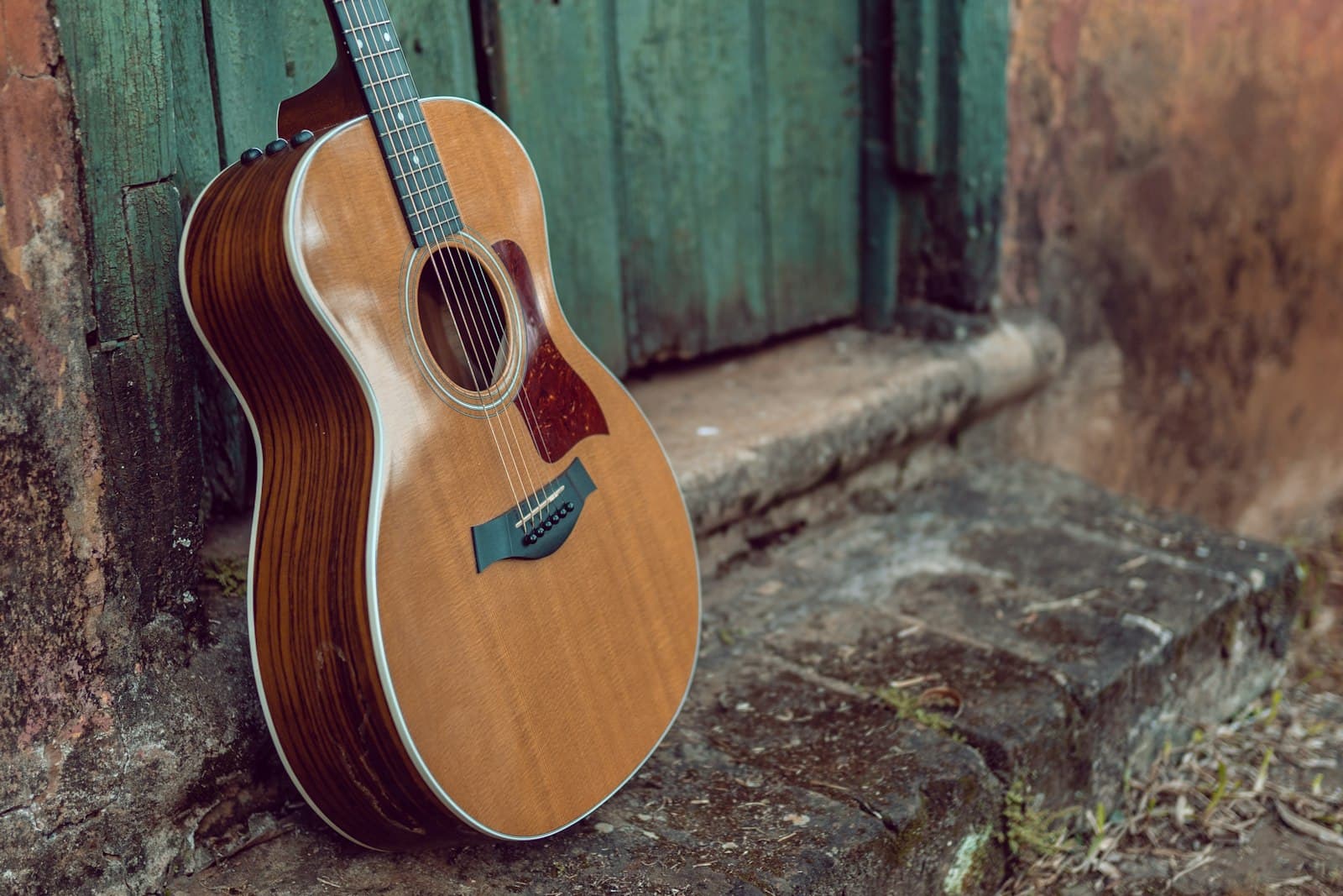 A honey-toned acoustic guitar leaning against a sunlit terracotta doorway